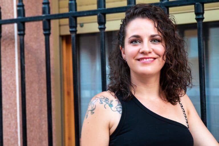Hermosa mujer con tatuaje en el brazo, sonriendo, en un entorno urbano alegre y luminoso.