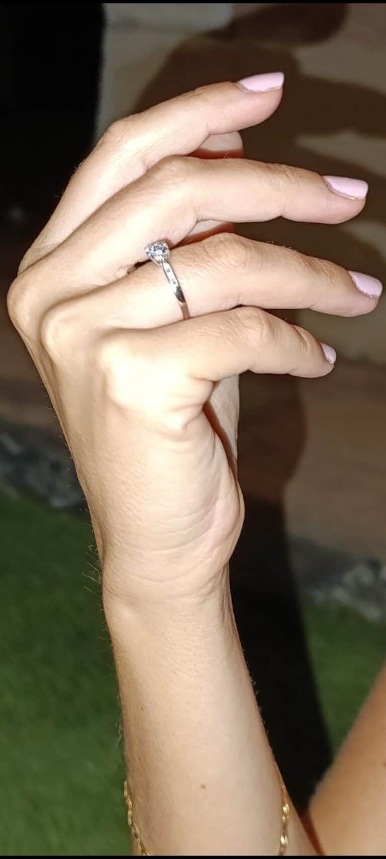 Yacente anillo de compromiso en mano con uñas pintadas en tonos rosados.